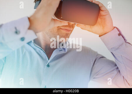 Closeup shot of businessman wearing virtual reality goggles against grey background. Young man using VR glasses with sun flare e Stock Photo
