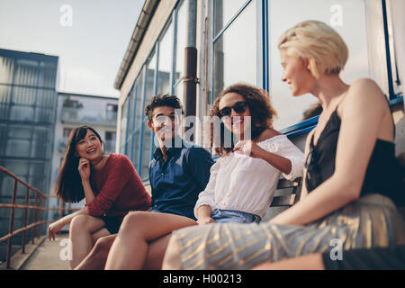 Shot of multiethnic group of friends sitting in balcony and talking. Young people relaxing outdoors in terrace and smiling. Stock Photo