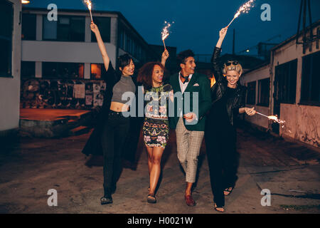 Full length shot of four young friends walking down the city street with fireworks and celebrating new years eve. Group of peopl Stock Photo
