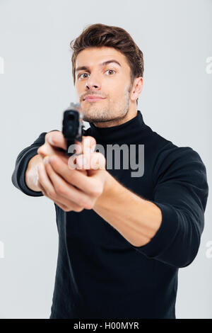 Serious young man standing and aiming gun on you Stock Photo