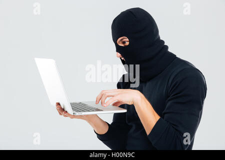 Portrait of man in balaclava standing and using laptop Stock Photo