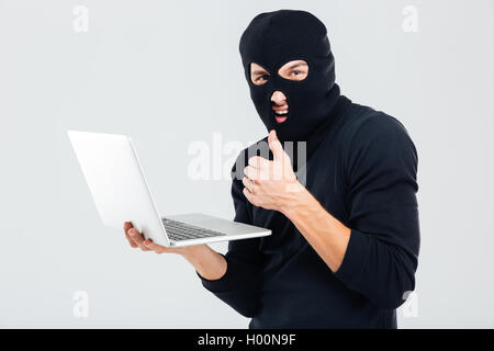 Man in balaclava using laptop and showing thumbs up Stock Photo