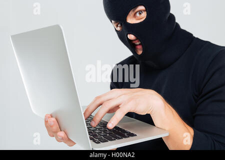 Closeup of criminal man in balaclava using laptop Stock Photo