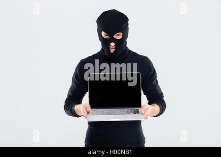 Criminal man in balaclava holding blank screen laptop Stock Photo