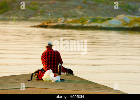 Marstrand, Sweden - September 8, 2016: Documentary of one man seen from behind sitting on pier looking at view while fishing. Th Stock Photo