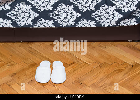 Slippers on wooden floor parquet in front on bed in house