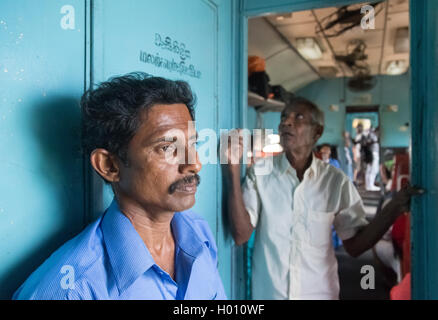 HIKKADUWA, SRI LANKA - MARCH 12, 2014: Two local men standing in train. Trains are very cheap and poorly maintained but it's the Stock Photo