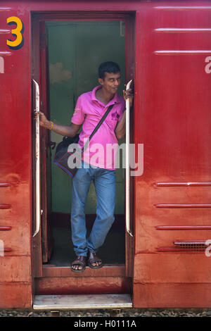 HIKKADUWA, SRI LANKA - MARCH 12, 2014: Local man standing at wagon entrance. Trains are very cheap and poorly maintained but it' Stock Photo