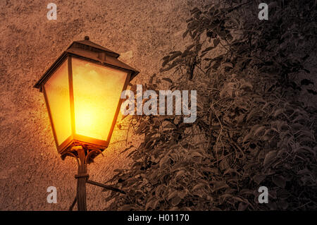 Cast iron wall mounted street lamp glowing in the dark with desaturated background Stock Photo