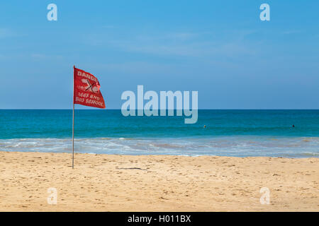 HIKKADUWA, SRI LANKA - FEBRUARY 24, 2014: Red danger flag waving in wind on sandy beach. Hikkaduwa is well known tourist interna Stock Photo