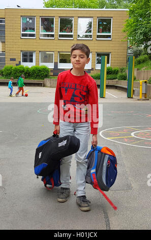 exhausted boy standing after end of school with satchel and guitar on the schoolyard Stock Photo