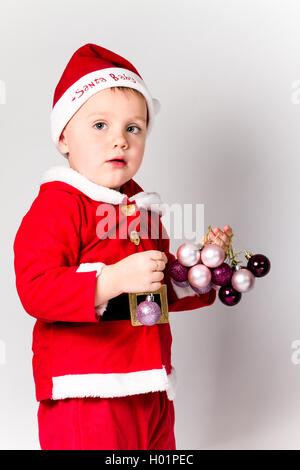 Baby boy dressed as Santa Claus holding Christmas baubles. White background. Stock Photo