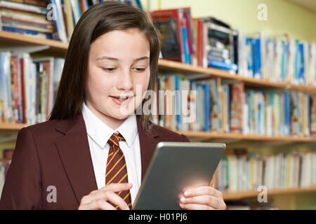 Girl Wearing School Uniform Using Digital Tablet In Library Stock Photo