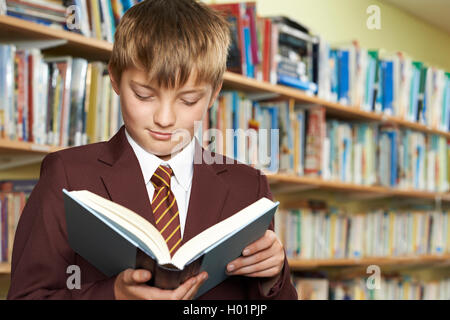 Boy Wearing School Uniform Reading Book In Library Stock Photo