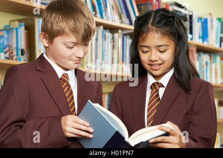 Pupils Wearing School Uniform Reading Book In Library Stock Photo