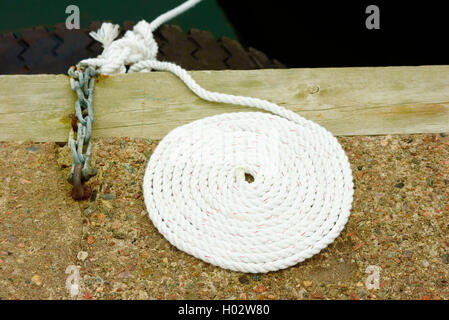 Coiled white rope on stone and wood pier. Stock Photo
