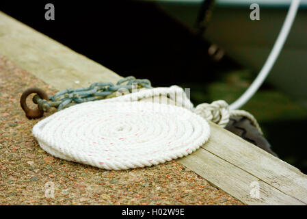 Coiled white rope on stone and wood pier. Stock Photo