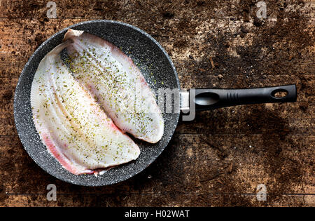 high-angle shot of a pair of raw flounders dressed with herbs in a frying pan, placed on a rustic wooden table Stock Photo