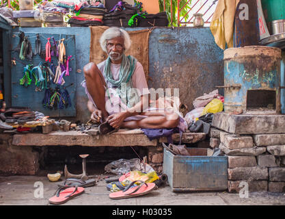 VARANASI, INDIA - 25 FEBRUARY 2015: Indian vendor sits in street shop and repairs slippers. Stock Photo