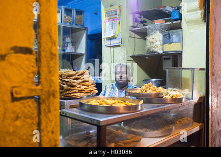 JODHPUR, INDIA - 16 FEBRUARY 2015: Vendor sits in store with food on metal plates. Stock Photo