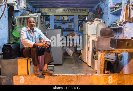 JODHPUR, INDIA - 10 FEBRUARY 2015: Elderly electrician sits on fridge before closing refrigerator service shop. Stock Photo