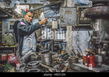 JODHPUR, INDIA - 07 FEBRUARY 2015: Indian mechanic works in workshop filled with scattered tools and machines. Post-processed wi Stock Photo