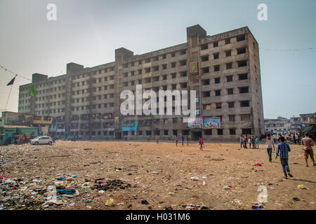 MUMBAI, INDIA - 12 JANUARY 2015: Unfinished empty apartment block and dirty field with people in Dharavi slum. Dharavi is one of Stock Photo