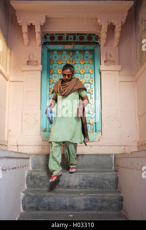 JODHPUR, INDIA - 07 FEBRUARY 2015: Woman in traditional clothes and scarf walking down stairs. Stone entrance and wooden door wi Stock Photo