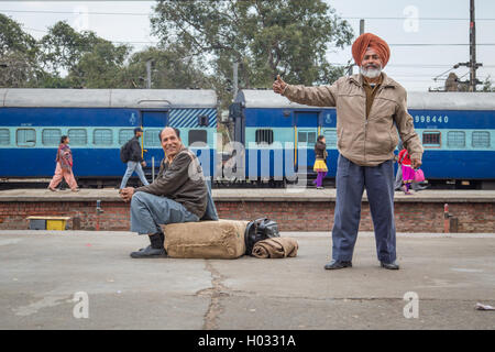 AMRITSAR, INDIA - 02 MARCH 2015: Elderly Sikh man shows thumbs up while other man laughs and sits on package on train platform. Stock Photo