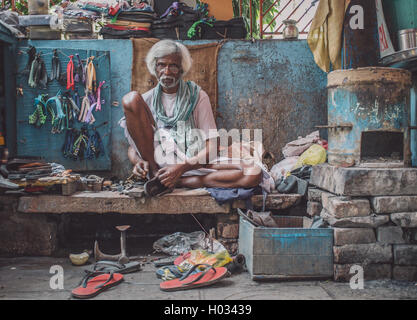VARANASI, INDIA - 25 FEBRUARY 2015: Indian vendor sits in street shop and repairs slippers. Post-processed with grain, texture a Stock Photo