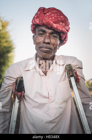 GODWAR REGION, INDIA - 12 FEBRUARY 2015: Rabari tribesman in field with crutches. Post-processed with grain, texture and colour  Stock Photo