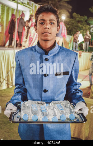 JODHPUR, INDIA - 08 FEBRUARY 2015: Young Indian boy wearing suit holds water bottles on tray working as waiter. Post-processed w Stock Photo