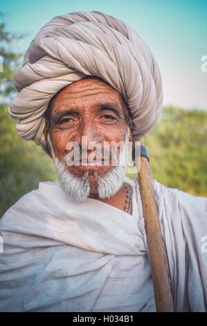 GODWAR REGION, INDIA - 14 FEBRUARY 2015: Elderly Rabari tribesman with white turban and blanket around the shoulders and ax. Pos Stock Photo