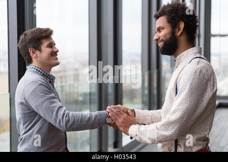 Two young businessmen shaking hands in modern office hall. Stock Photo