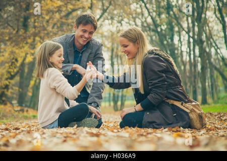 Family of three kneel in park on an autumn day. Stock Photo