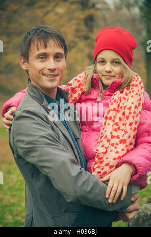 Young father holds daughter in hands. Daughter wears jacket, hat and scarf. Stock Photo