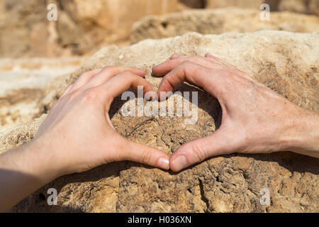 Man and woman making heart shape with their hands on rock. Stock Photo