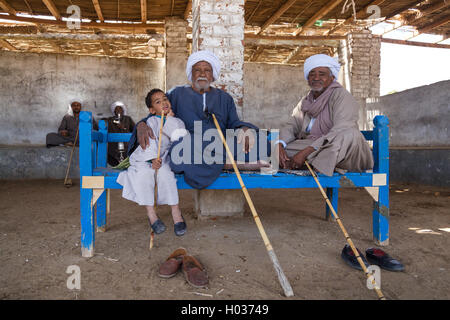 DARAW, EGYPT - FEBRUARY 6, 2016: Two elderly camel salesmen and little boy sitting on the bench at Camel market. Stock Photo
