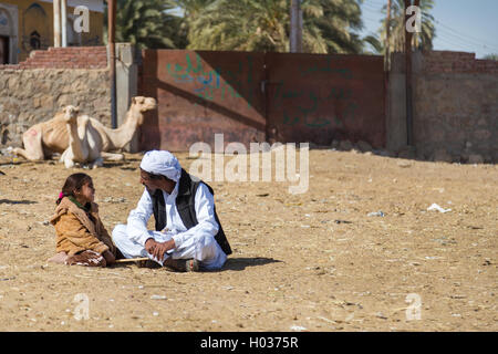 DARAW, EGYPT - FEBRUARY 6, 2016: Local camel salesmen and little girl sitting on the ground at camel market. Stock Photo