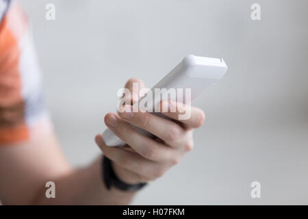 Young man holding white mobile phone in hand, using smartphone app, scrolling, close-up Stock Photo