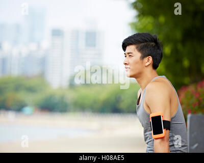 young handsome asian jogger wearing fitness tracker taking a break in a city park Stock Photo