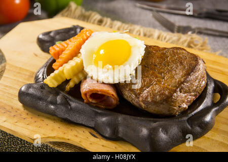 Beefsteak on iron plate with egg and carrot on the table in restautrant Stock Photo