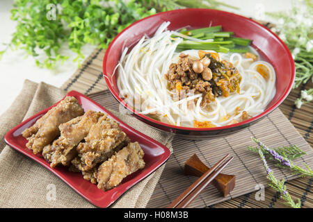 Chinese bowl of noodle with fried pork ribs and herbs on the table Stock Photo