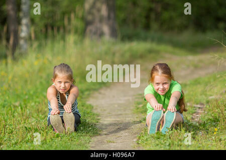 Two little girls perform gymnastic exercises outdoors. Stock Photo