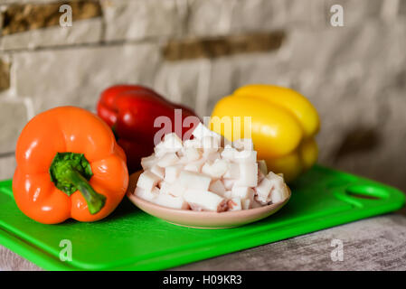 Lard cubes in small plate with colored bell peppers on green plastic board Stock Photo