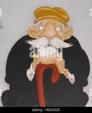 Wall art of kindly old man with white beard and big moustache, in black clothes and beret, sitting leaning on walking stick Stock Photo
