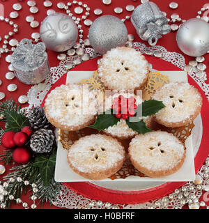 Traditional christmas mince pie cakes with silver bauble decorations, holly and winter greenery on red background. Stock Photo