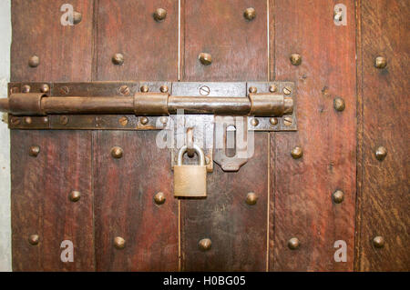 Closeup of a brass hinge and padlock on rustic wooden door with patterned bolts embedded. Stock Photo