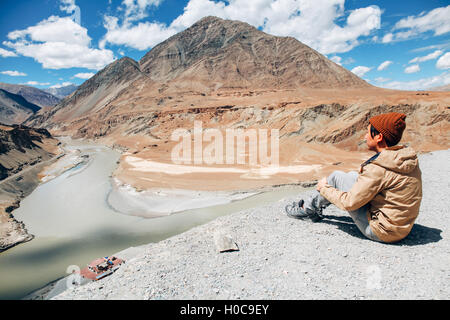 Young happy man sitting on the cliff on the trip in Indus River in Leh, Ladakh, India Stock Photo