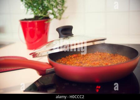Vegetarian lentil bolognese sauce in a frying red pan on a dark stove Stock Photo
